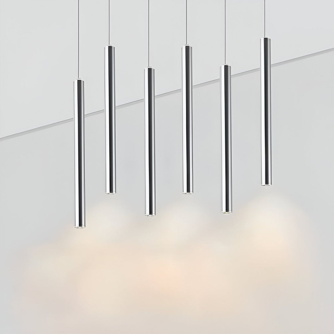 L'image représente une rangée de cinq suspensions lumineuses cylindriques en métal de couleur argentée. Les suspensions sont disposées à intervalles réguliers et émettent une lumière chaude.