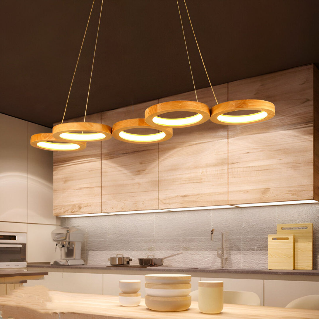 Une suspension en bois avec cinq anneaux de différentes tailles. La suspension est accrochée au plafond par des fils fins. Les anneaux sont en bois clair et diffusent une lumière chaude. La suspension est idéale pour une salle à manger ou un salon. EL-1630698474,EL-3714136010,EL-2272764185,EL-0448510413,