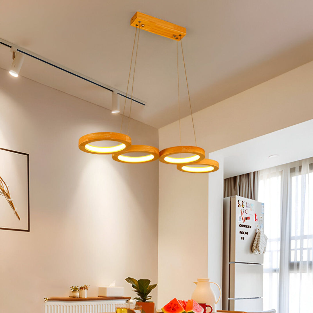 Une suspension en bois avec quatre cercles en bois qui diffusent une lumière chaude. La suspension est accrochée à un plafond blanc. EL-1630698474,EL-3714136010,EL-2272764185,EL-0448510413,