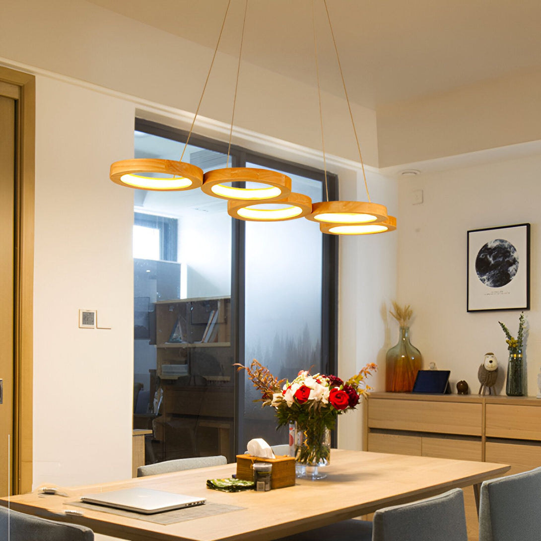 Une suspension en bois avec cinq anneaux lumineux. La suspension est fixée au plafond par un câble. Les anneaux sont en bois et ont une forme ronde. Ils sont disposés de manière à former un cercle. La suspension est éclairée par des LED. EL-1630698474,EL-3714136010,EL-2272764185,EL-0448510413,