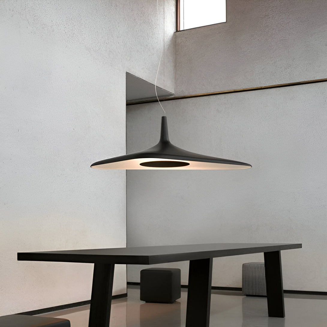 Une image d'une lampe noire en forme de soucoupe volante suspendue au plafond. La lampe est éclairée et diffuse une lumière blanche. La pièce est blanche et épurée. Il y a une table en bois avec des chaises autour. FE-0845784005,FE-6341289162,FE-2159944122,FE-9984768821,