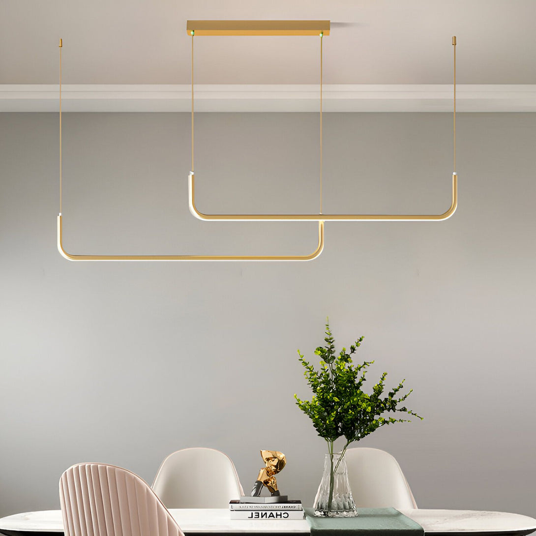 Une image d'une suspension LED moderne en forme de U doré. La suspension est fixée au plafond par deux câbles fins et émet une lumière blanche chaude. En dessous, il y a une table à manger avec des chaises et un vase avec des fleurs vertes. CU-6987275459,CU-2256173763,CU-8965480825,CU-2593177039,CU-6967884158,CU-8028259170,CU-425617155X,CU-8536488247,CU-0217384609,CU-6824179981,CU-5339287629,CU-8508221142,