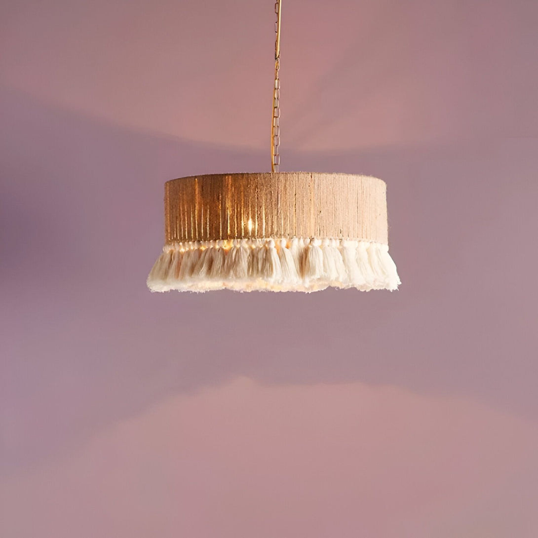Un lustre rond en corde avec des pampilles blanches est suspendu à une chaîne dorée. Le lustre est allumé et émet une lumière chaude. Le fond est rose. BE-3772910335,BE-6814217791,BE-5486832621,BE-1720615667,BE-4673989724,BE-7949774487,