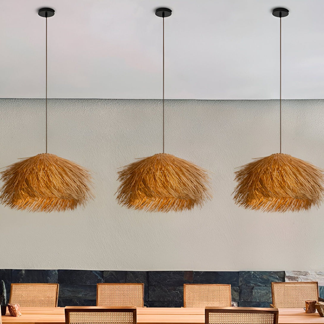 Une image de trois lampes suspendues en paille tressée. Les lampes sont de forme ronde et ont une frange de paille qui pend du bas. Les lampes sont suspendues à des fils noirs et sont fixées à un plafond blanc. Il y a une table en bois avec des chaises en osier en dessous des lampes.