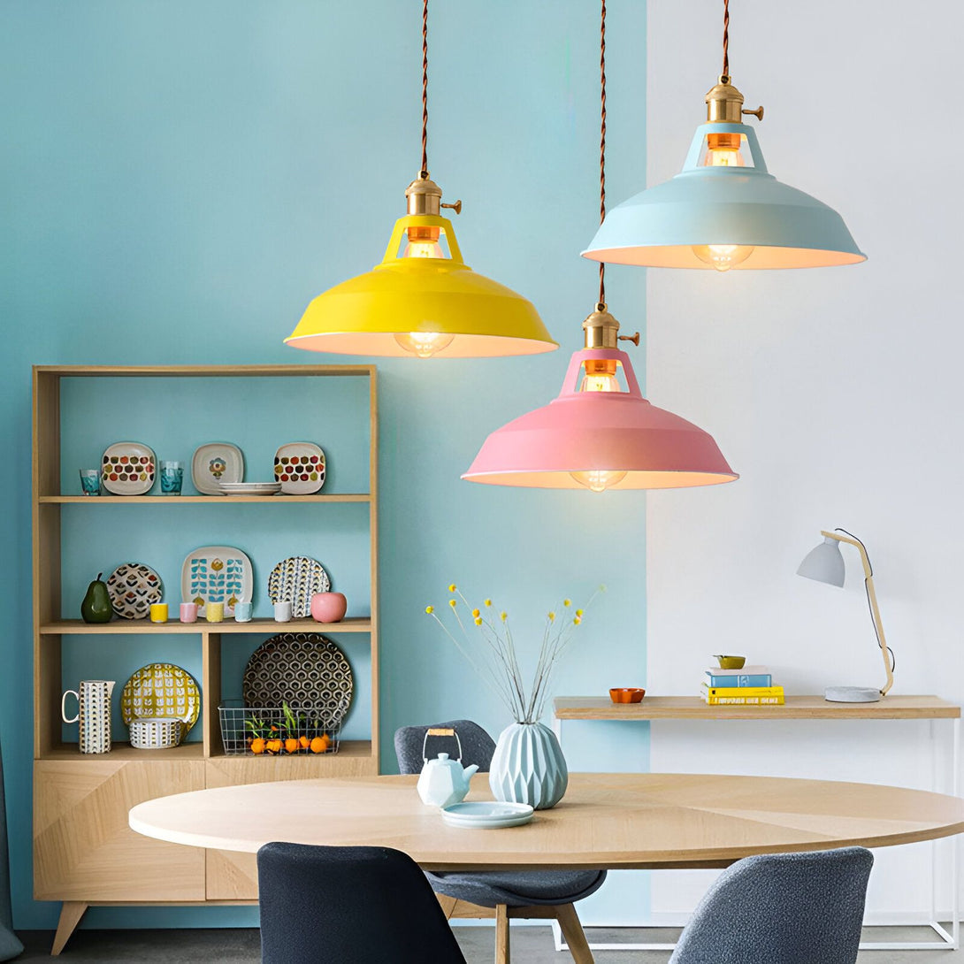 Trois suspensions colorées en métal avec des fils électriques apparents. Les suspensions sont de couleurs différentes : jaune, bleu et rose. Elles sont disposées au-dessus d'une table à manger en bois. FA-089456174X,FA-0854347186,FA-3722436486,FA-9208232328,FA-854769725X,FA-3347333489,FA-9646103529,
