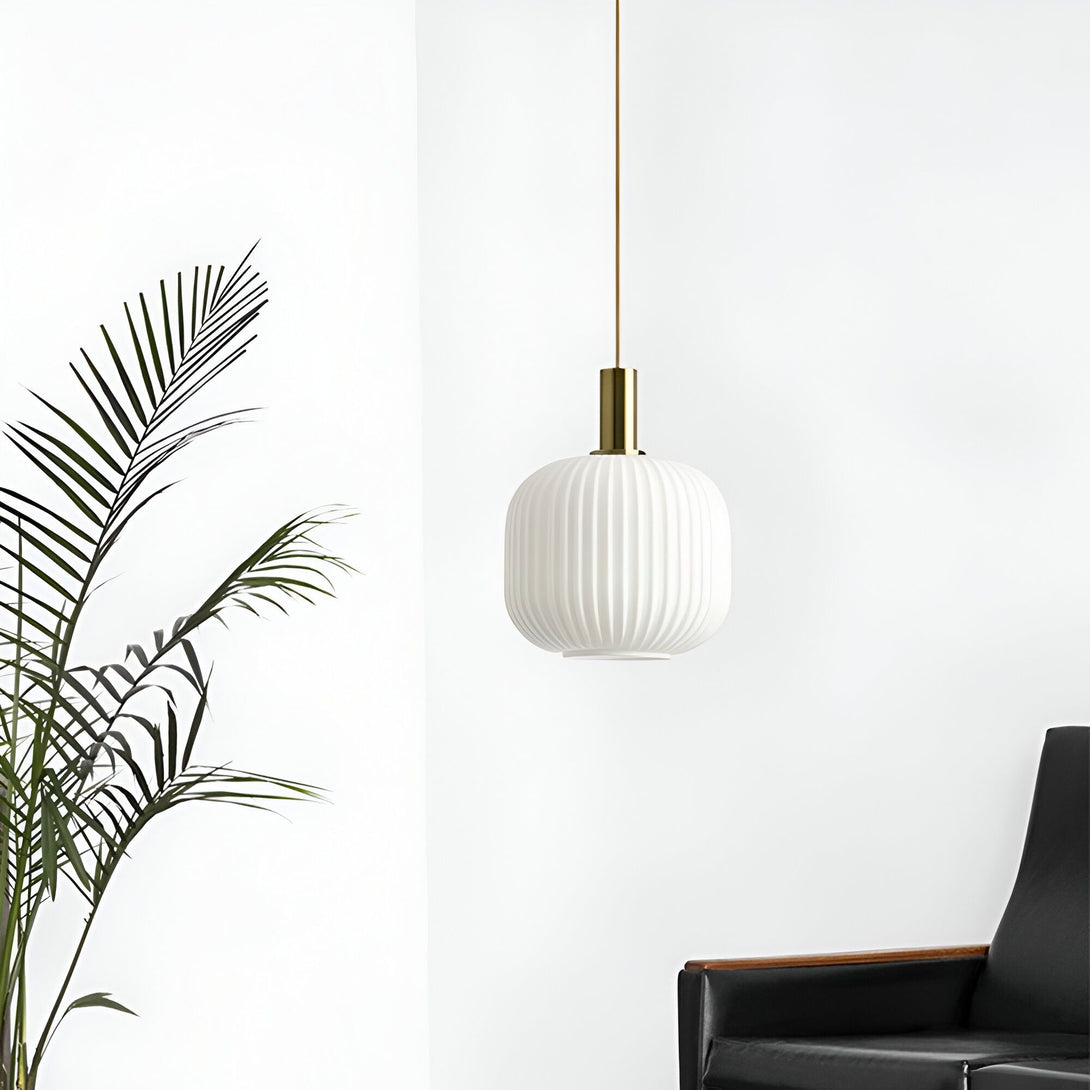 Une image d'une lampe à suspension en verre blanc avec un cordon en laiton. La lampe est suspendue au-dessus d'un fauteuil en cuir noir. À côté de la lampe, se trouve un palmier. LI-8529220781,LI-4720739318,LI-9433830652,LI-6287765305,