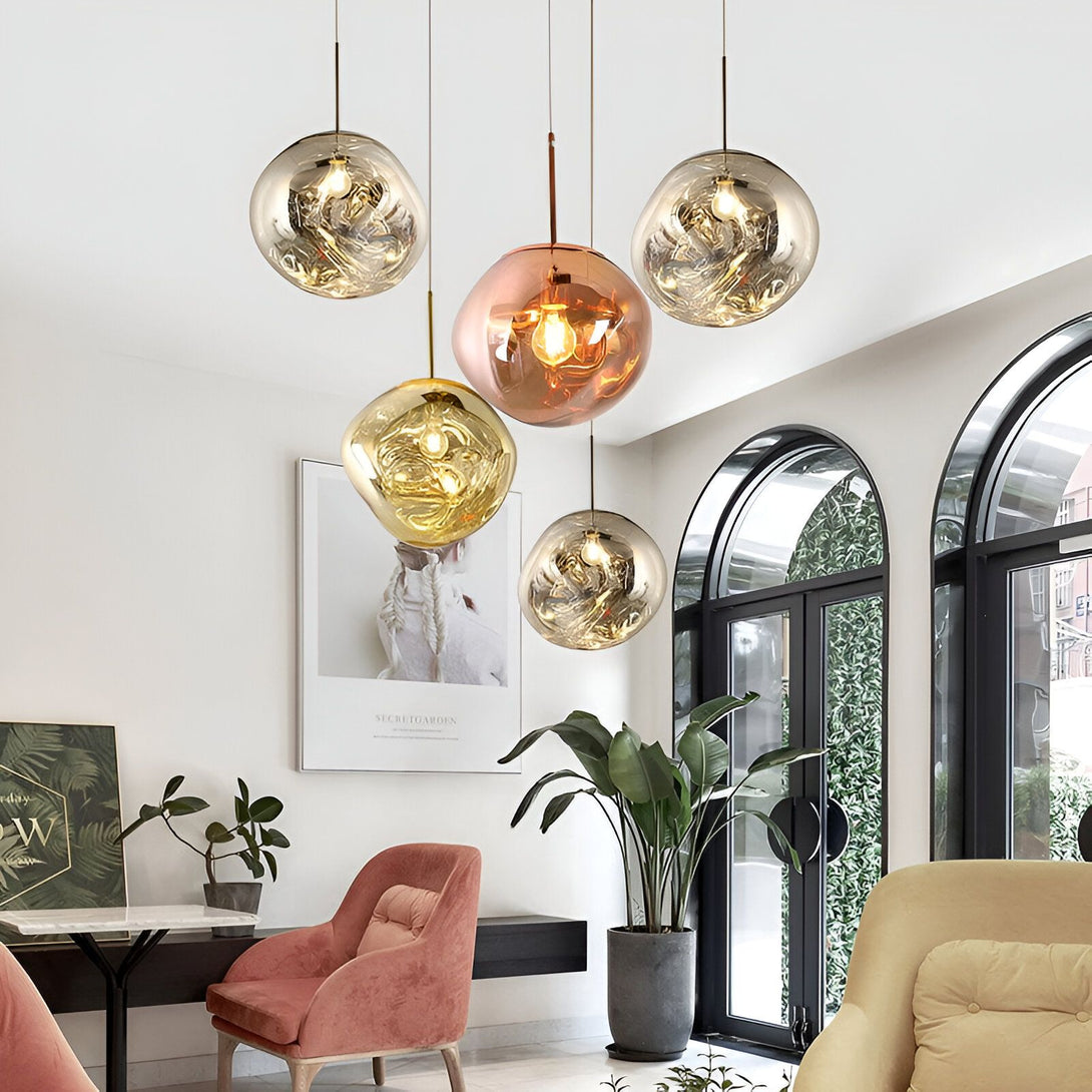 Une image de cinq lampes à suspension en verre soufflé de différentes couleurs. Les lampes sont suspendues à des fils métalliques fins et sont allumées. Il y a un mur blanc en arrière-plan et un sol en marbre. LA-8821800008,LA-2444977270,LA-6285199337,LA-272961009X,LA-427140456X,LA-929285948X,LA-4420956534,LA-5212907888,LA-5689243493,