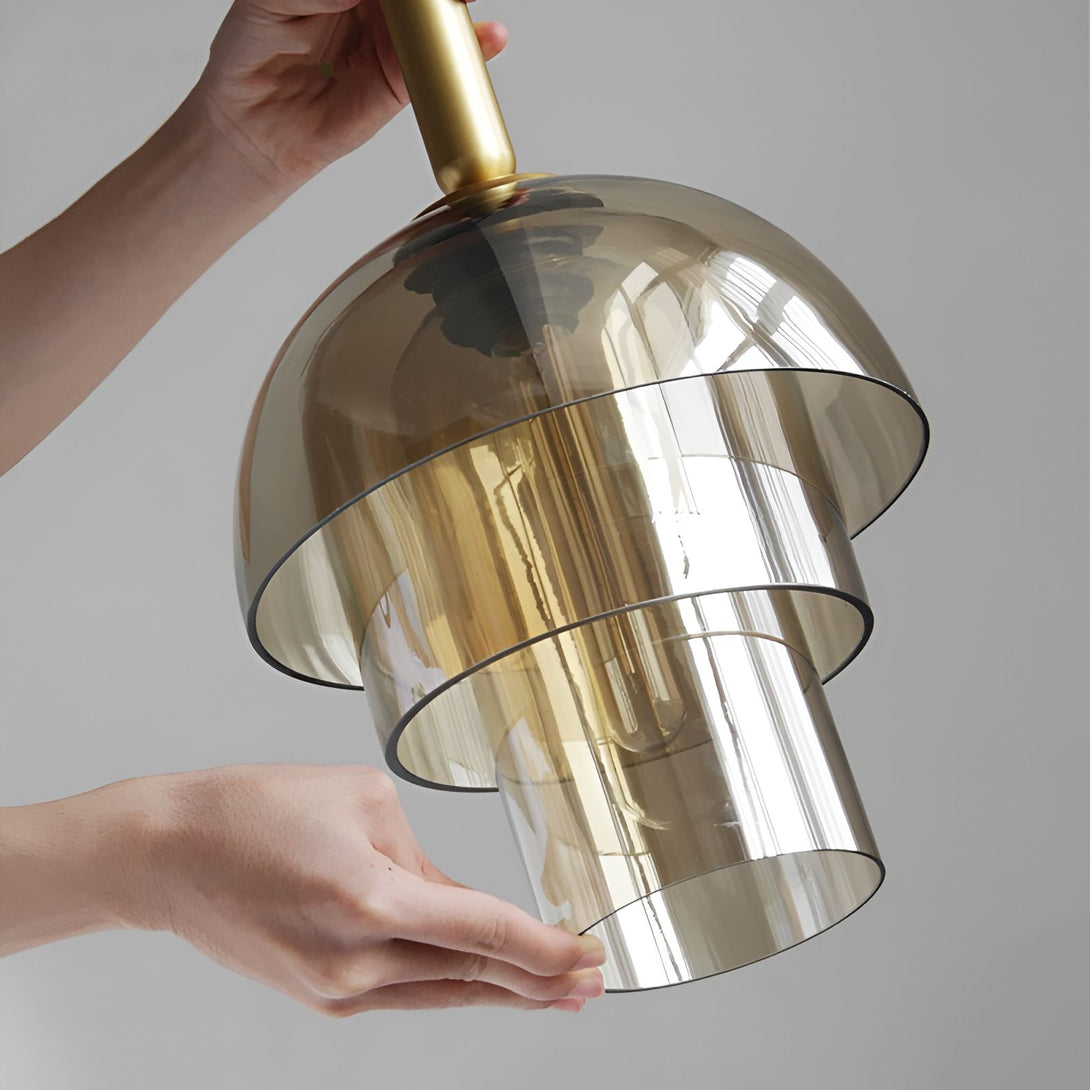 Une main tenant une lampe en verre doré. La lampe est composée de trois parties en verre fumé et doré. LA-8544977014,LA-4041186528,